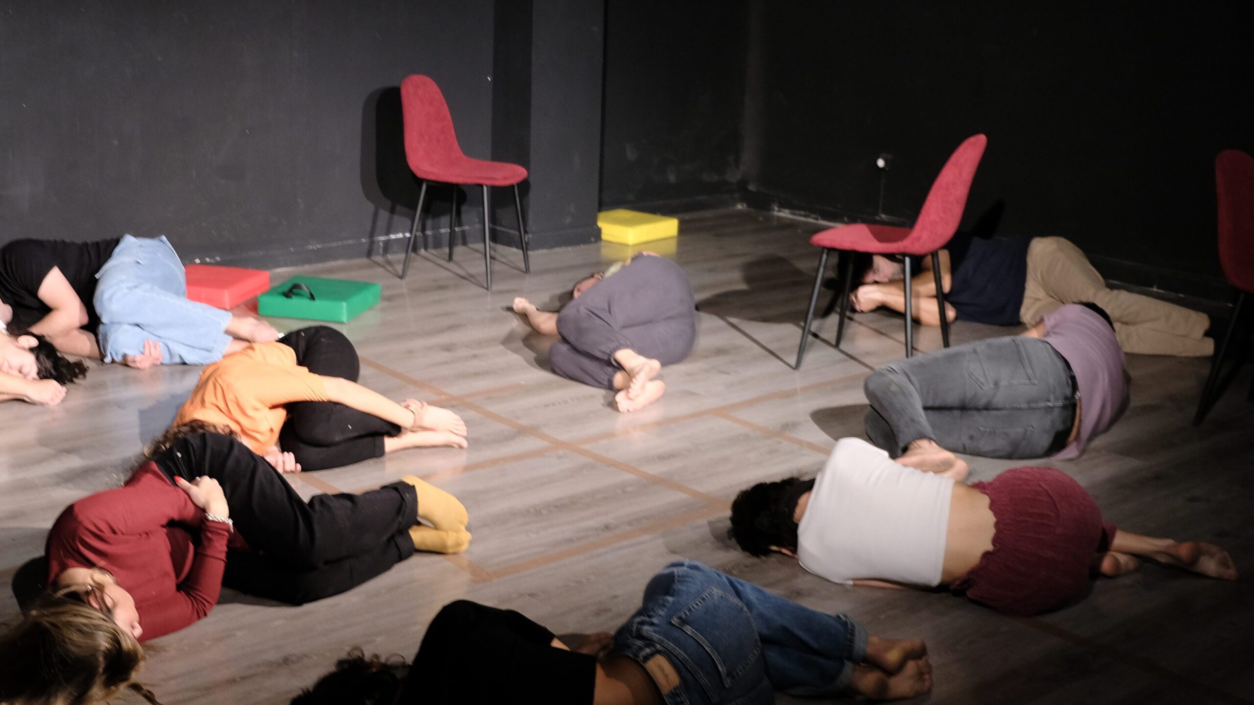 chicos en clase de teatro tumbados en el suelo a media luz