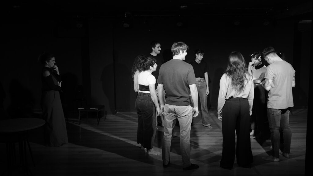 Alumnos estudiantes de teatro en una ronda con la profesora mirando. Foto en blanco y negro